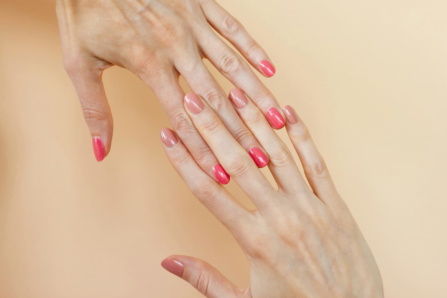 Verzorgde handen met een elegante roze BIAB manicure op een warme zandkleurige achtergrond